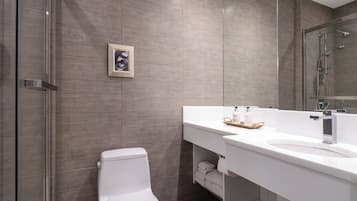 Un baño moderno con cabina de ducha de vidrio, inodoro blanco y tocador con espejo y dos botellas de champú.