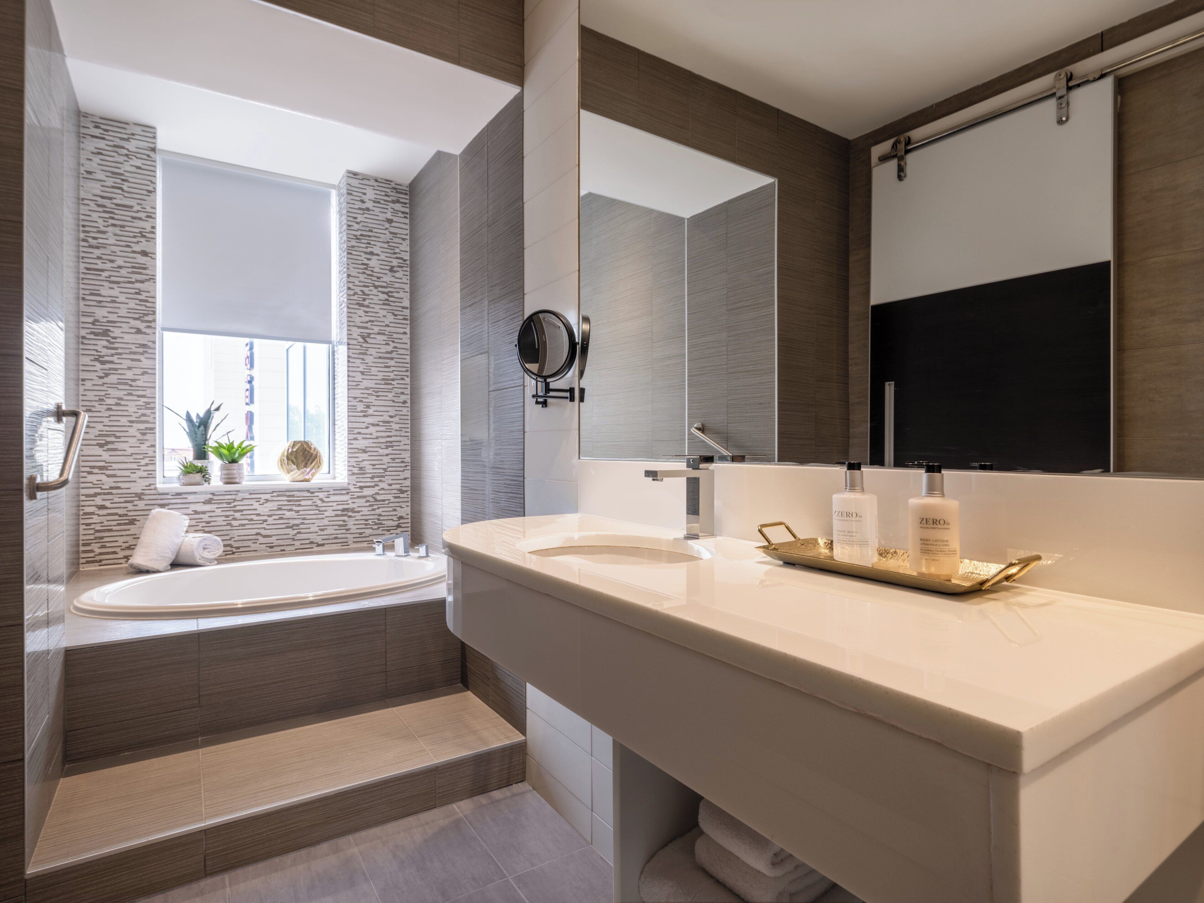 Une salle de bain moderne avec une baignoire sur pieds, un grand miroir et un meuble-lavabo doté d’un plateau pour ranger les articles de toilette.