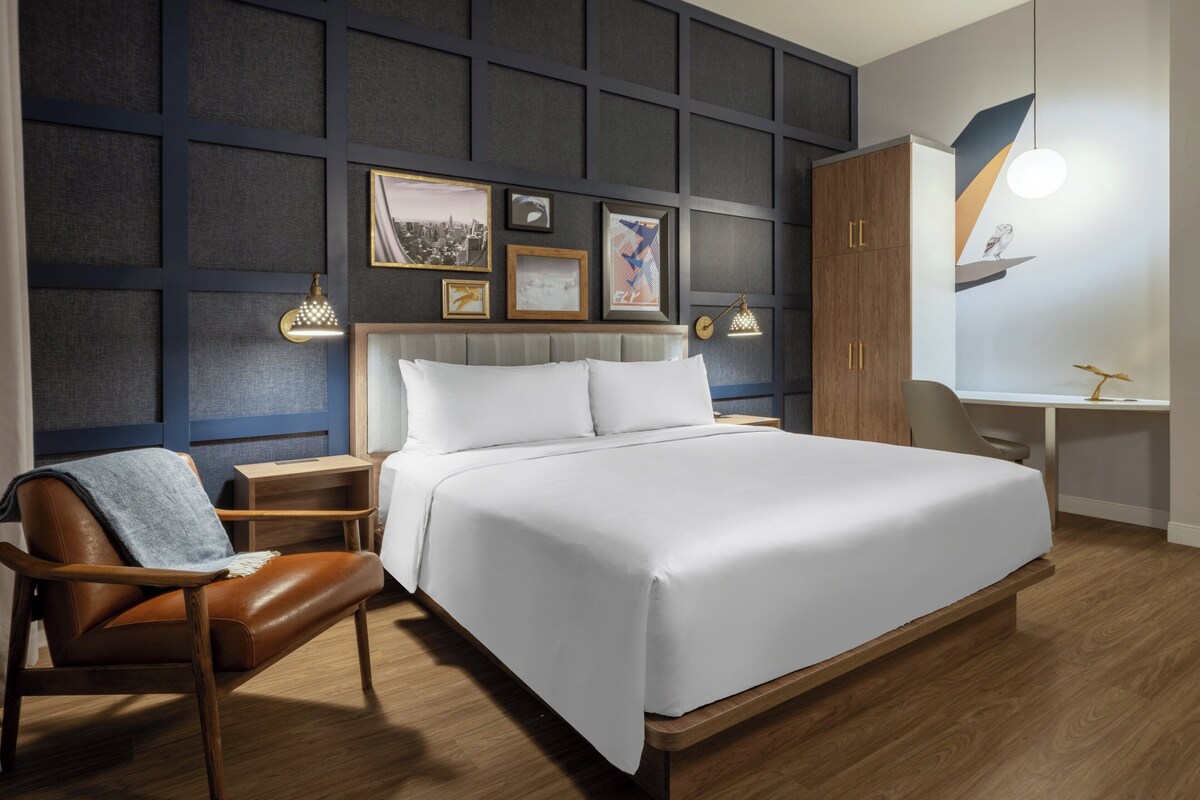 Ein modernes Schlafzimmer mit einem großen Bett, einem Schreibtisch und einem Stuhl. An den Wänden sind Lampen und gerahmte Bilder angebracht.