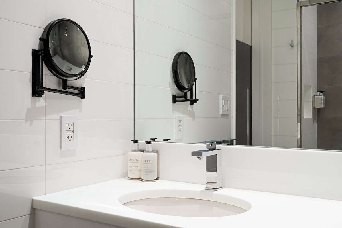 Casa de banho moderna com lavatório branco, dois espelhos redondos e duas embalagens de loção para as mãos.
