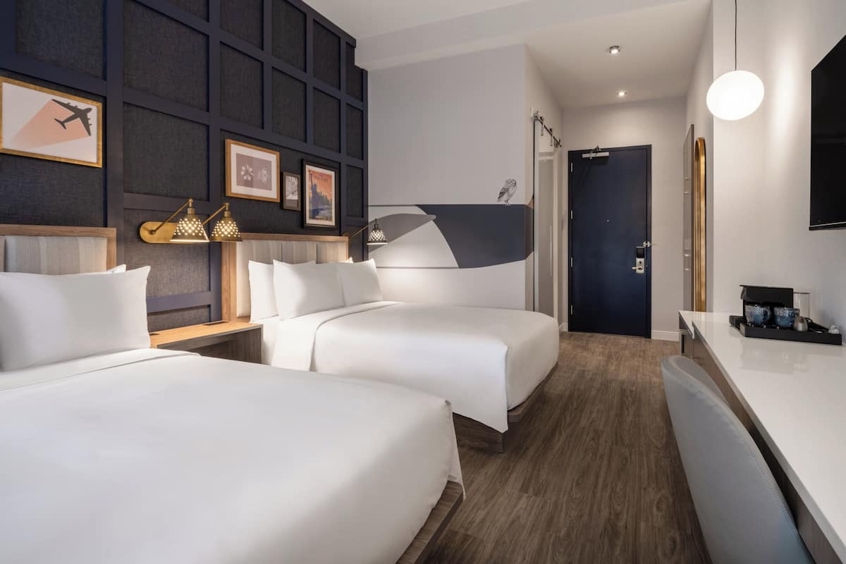 Een moderne hotelkamer met twee bedden, een bureau en een donkerdeur.
