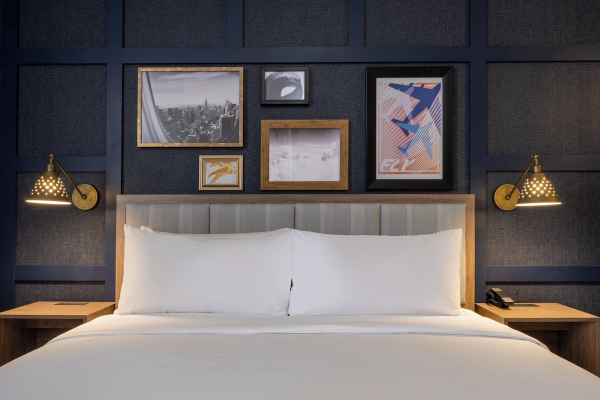 Een hotelkamer met een groot bed, een hoofdbord en een muur versierd met ingekaderde foto’s en twee wandlampen.