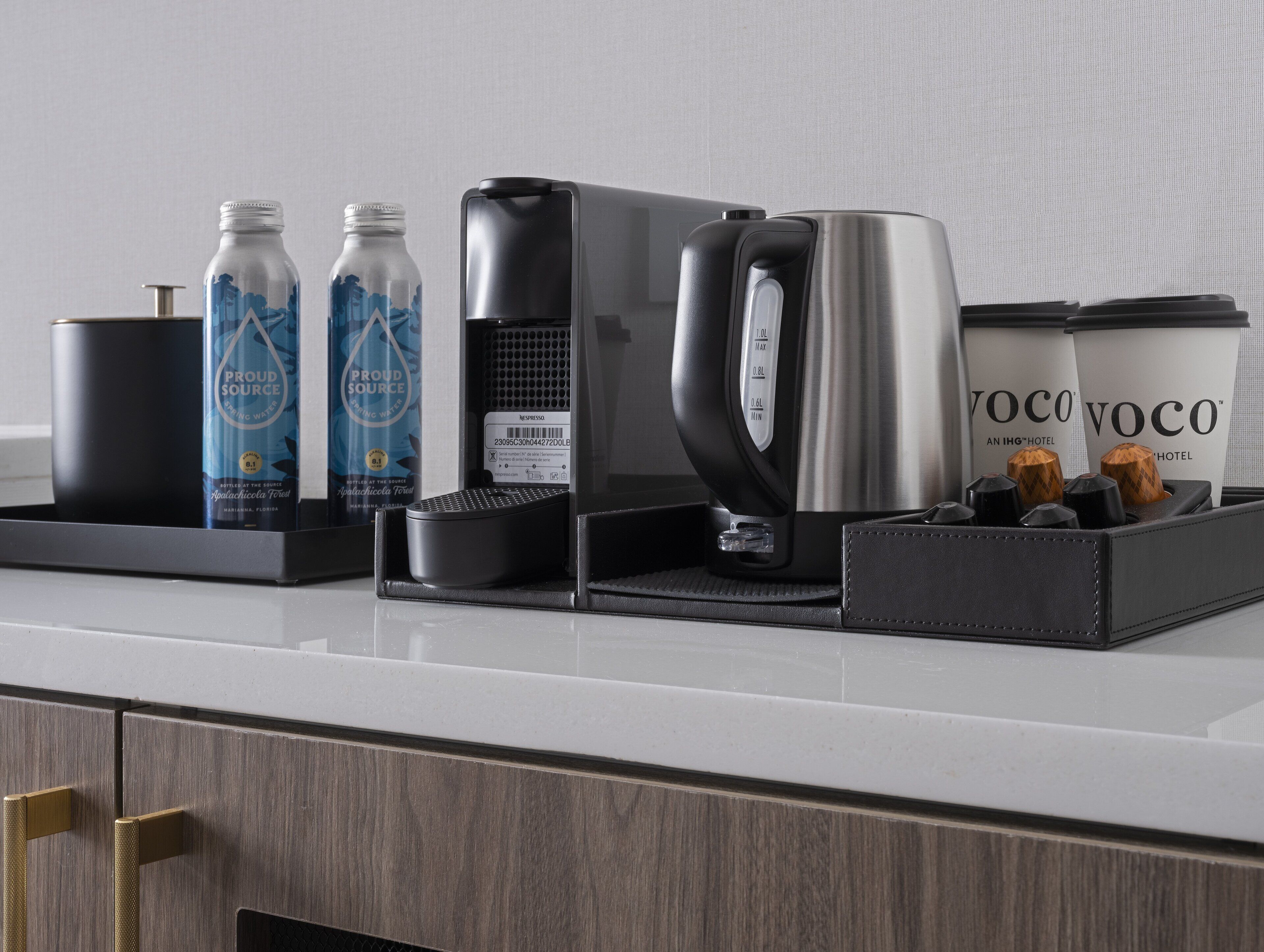 Een koffiehoek met een koffiezetapparaat, waterflessen en een koffiekan op een aanrecht.