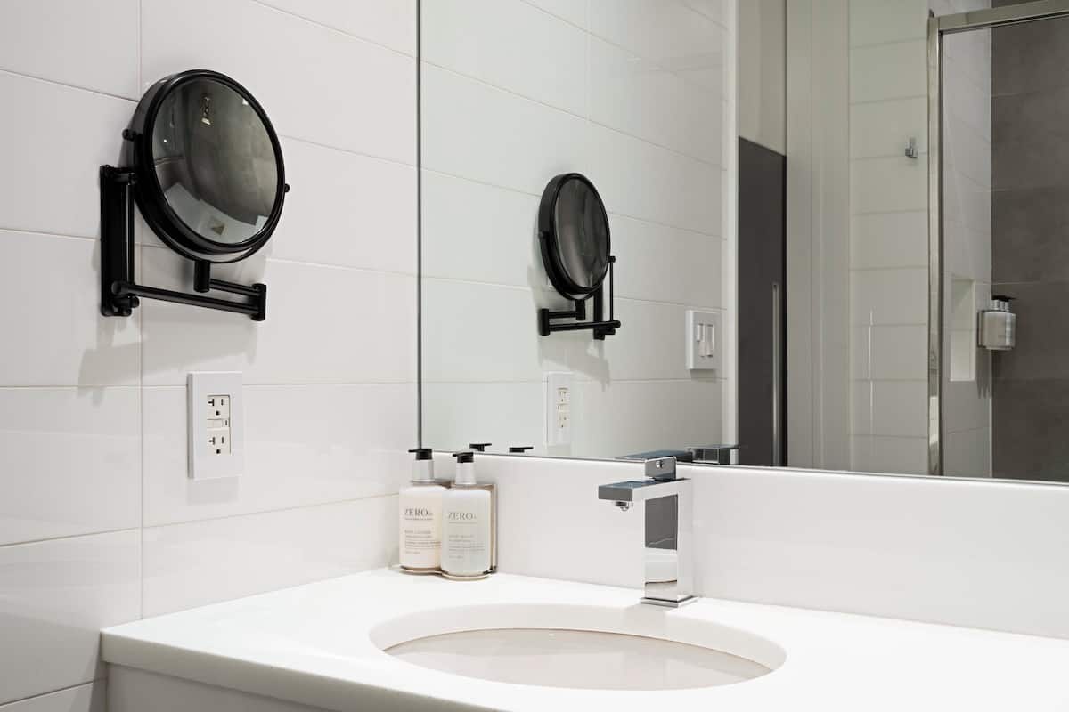 Een moderne badkamer met een witte wasbak, twee ronde spiegels en twee flesjes handcrème.