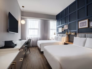 Een hotelkamer met twee bedden, een bureau, een flatscreentelevisie en een groot raam met dunne gordijnen.
