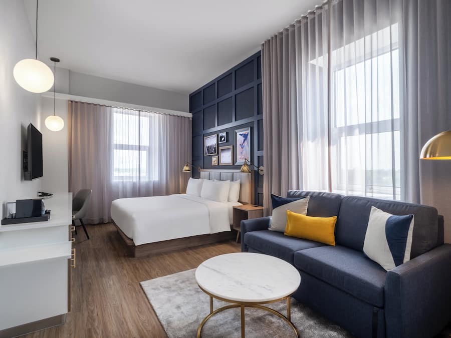 A modern hotel room with a bed, a sofa, a desk, and a television.