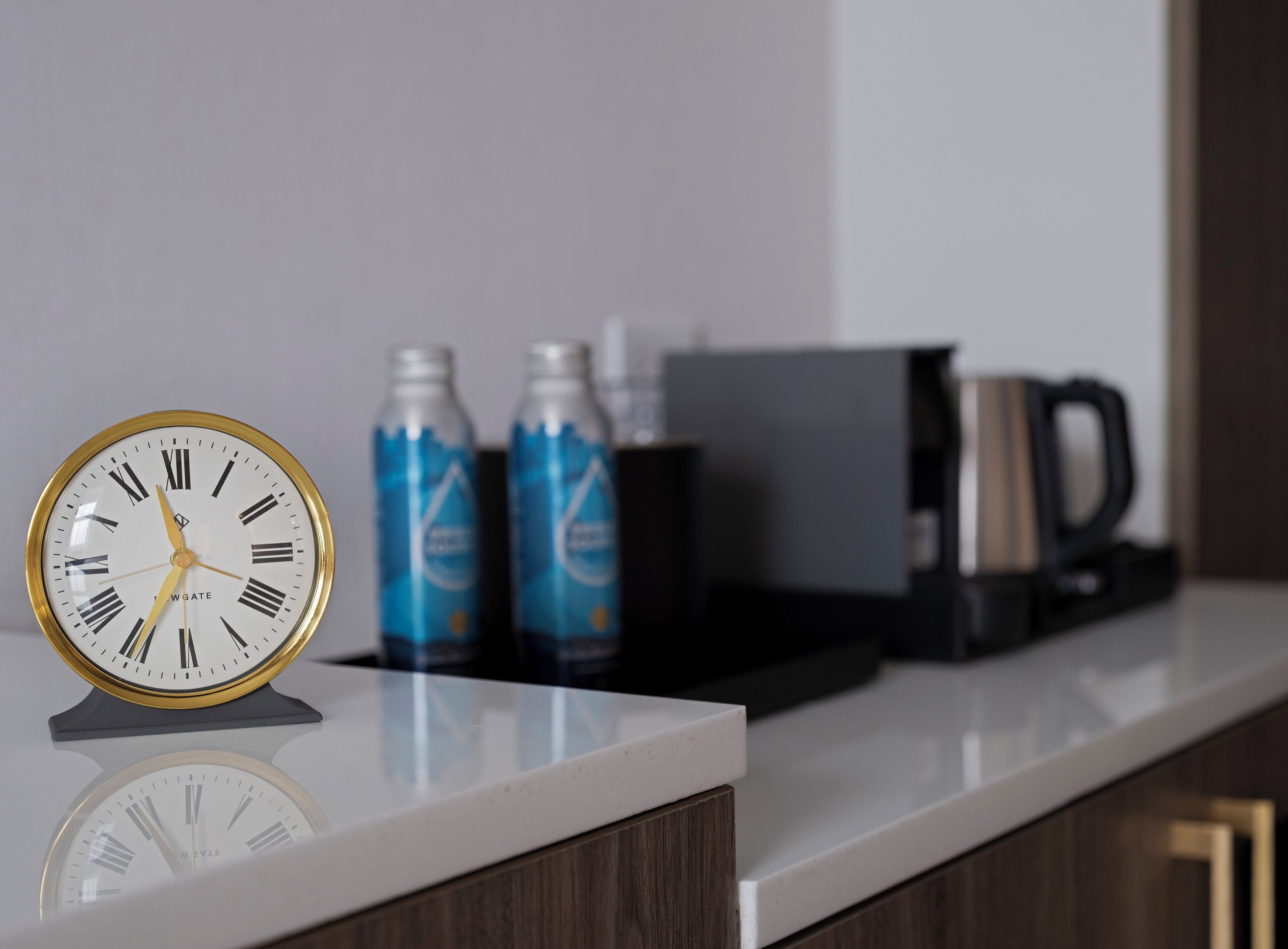 A kitchen counter with a clock, two water bottles, and a coffee maker.