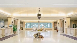 Un hall d’entrée spacieux, doté d’une table ronde centrale où sont exposés des objets décoratifs, d’un lustre et d’un comptoir de réception avec un ordinateur.