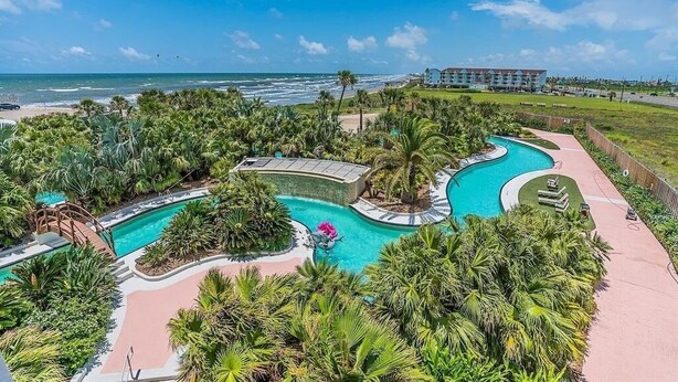Un complexe hôtelier doté d’une grande piscine, de palmiers et offrant une vue sur l’océan.
