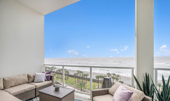 A balcony with a view of the ocean, a sofa, a coffee table, and a potted plant.