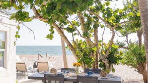 An outdoor dining area with a table and chairs, surrounded by trees and a view of the beach. - "Lost Loon" Oceanfront Cottage by Roxy Rentals (Englewood)