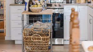 A kitchen with white cabinets, a microwave, a stove, and a wicker basket on a cart. - "Lost Loon" Oceanfront Cottage by Roxy Rentals (Englewood)