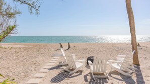 A beach with white Adirondack chairs and a wooden walkway leading to the water. - "Lost Loon" Oceanfront Cottage by Roxy Rentals (Englewood)