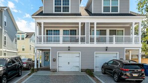 En tvåvånings bostadsbyggnad med en veranda på framsidan, två garage och en balkong.