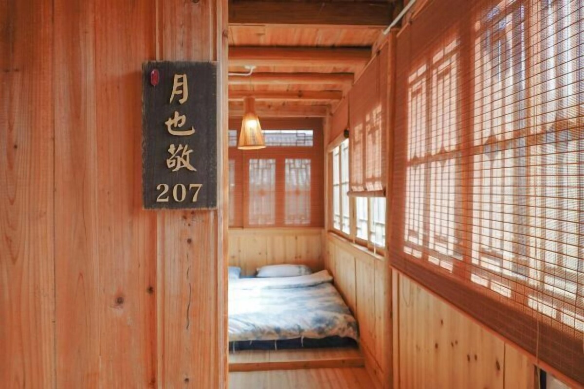 A wooden interior with a bed, a hanging light, and a window with a grid pattern.