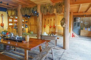 Un interior rústico de madera con una larga mesa de comedor, bancos y estantes llenos de diversos objetos.
