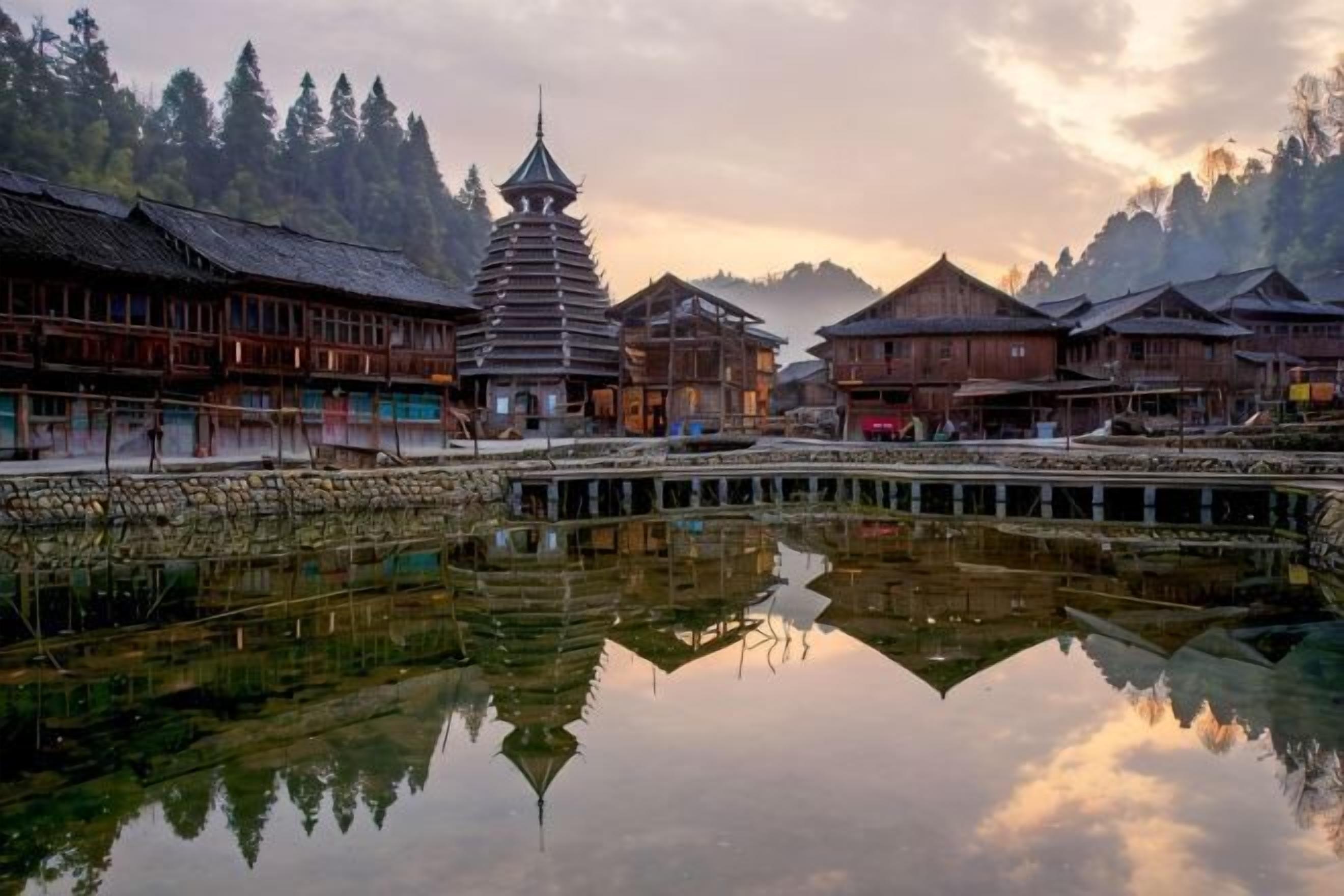 Un edificio de madera tradicional con una torre de estilo pagoda, un reflejo en aguas tranquilas y montañas boscosas al fondo.