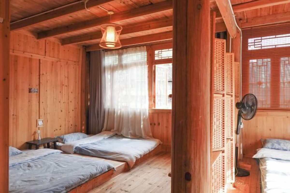 Een houten kamer met twee bedden, een ventilator en een raam met gordijnen.