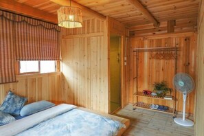 A wooden cabin room with a bed, a fan, a shelf with shoes, and a window with curtains. - Yueyetang Inn(Liping Huanggang Dong nationality Branch) (Liping)