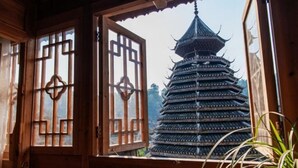 Une pagode traditionnelle à plusieurs niveaux, vue à travers une porte en bois ornée de motifs géométriques.