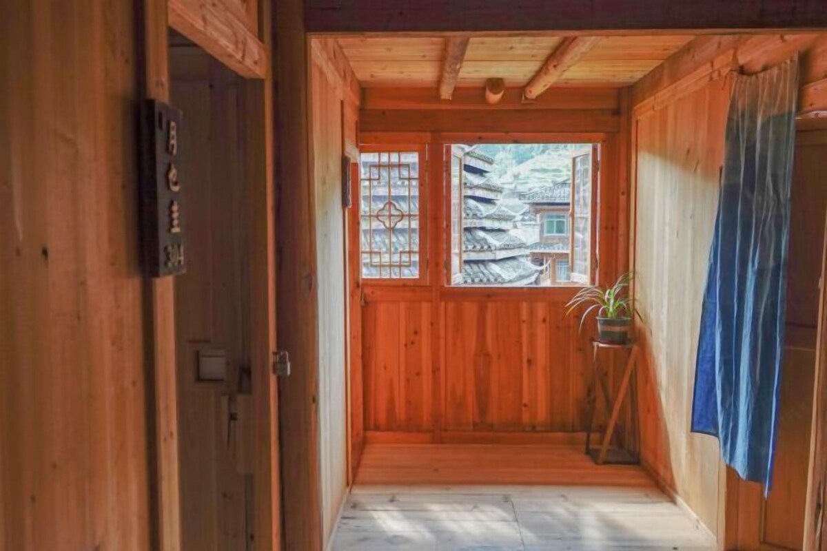 A wooden interior with a traditional Japanese-style sliding door, a small wooden stool with a plant, and a view of a pagoda through the door.