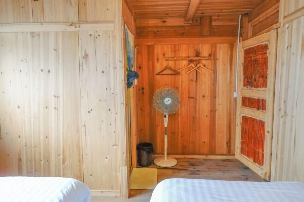 A wooden room with a bed, a fan, and a door with a window.