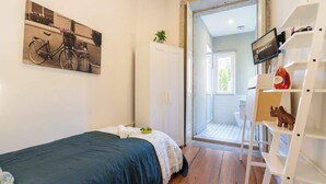 Quarto com cama, pintura de bicicleta, guarda-roupa, televisão e prateleira branca com objetos.