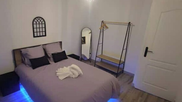 A bedroom with a bed, a bedside table, a hanging chair, a mirror, and a door. - Le Bill'ppart Easy Life (Bourgoin-Jallieu)