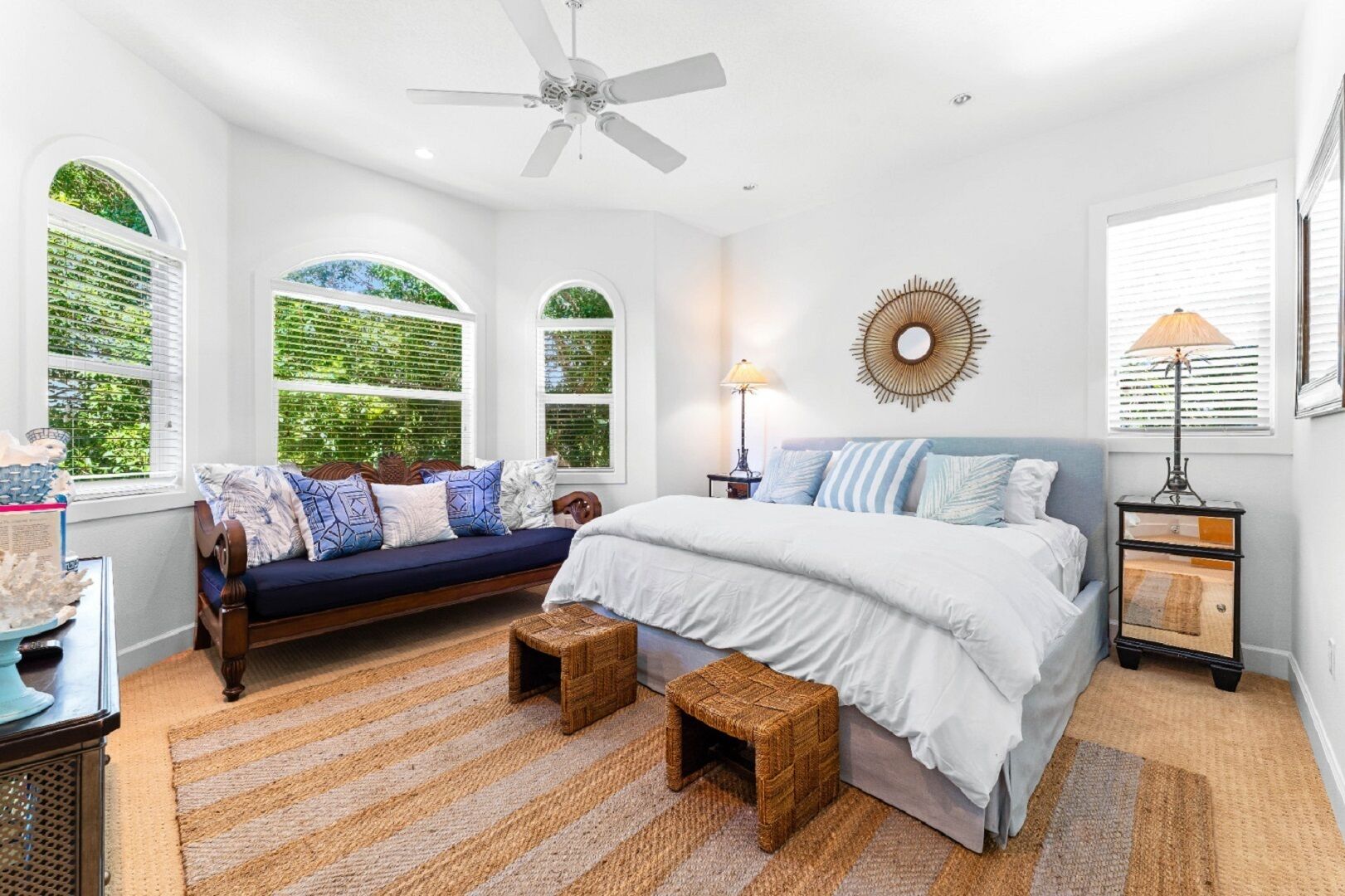 Une chambre avec un grand lit, un canapé, un ventilateur de plafond et une vue sur la verdure par les fenêtres.