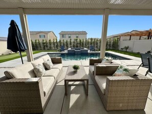 A covered outdoor area with wicker furniture, a pool, and a view of houses in the background. - Desert Azure - Horse Show, Karaoke, Air Hockey (Coachella)