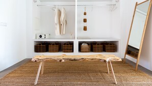 A room with a large mirror, a wooden bench, and shelves with baskets and hanging clothes. - Cenoura-Brava Villas & Suites. (Évora)