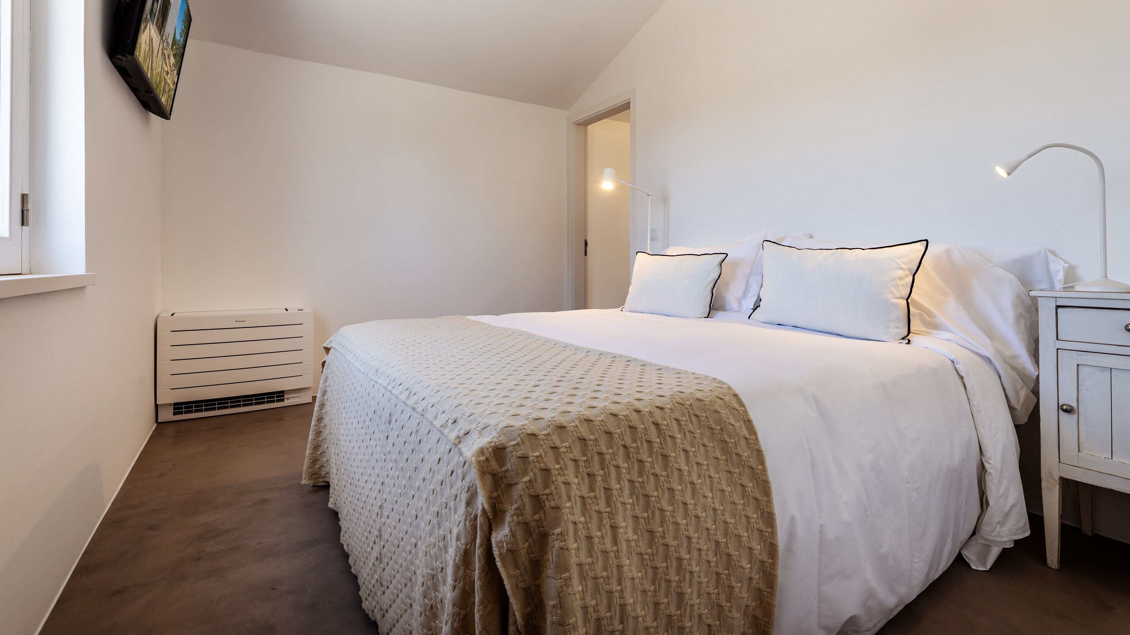 A bedroom with a bed, bedside table, lamp, and a wall-mounted TV.