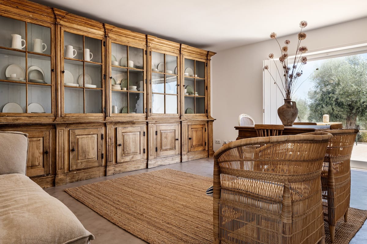 A living room with a large wooden cabinet, a wicker chair, and a view of the outdoors.