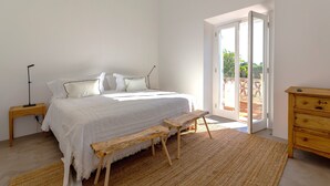 A bedroom with a large bed, wooden bench, and a dresser. - Cenoura-Brava Villas & Suites. (Évora)