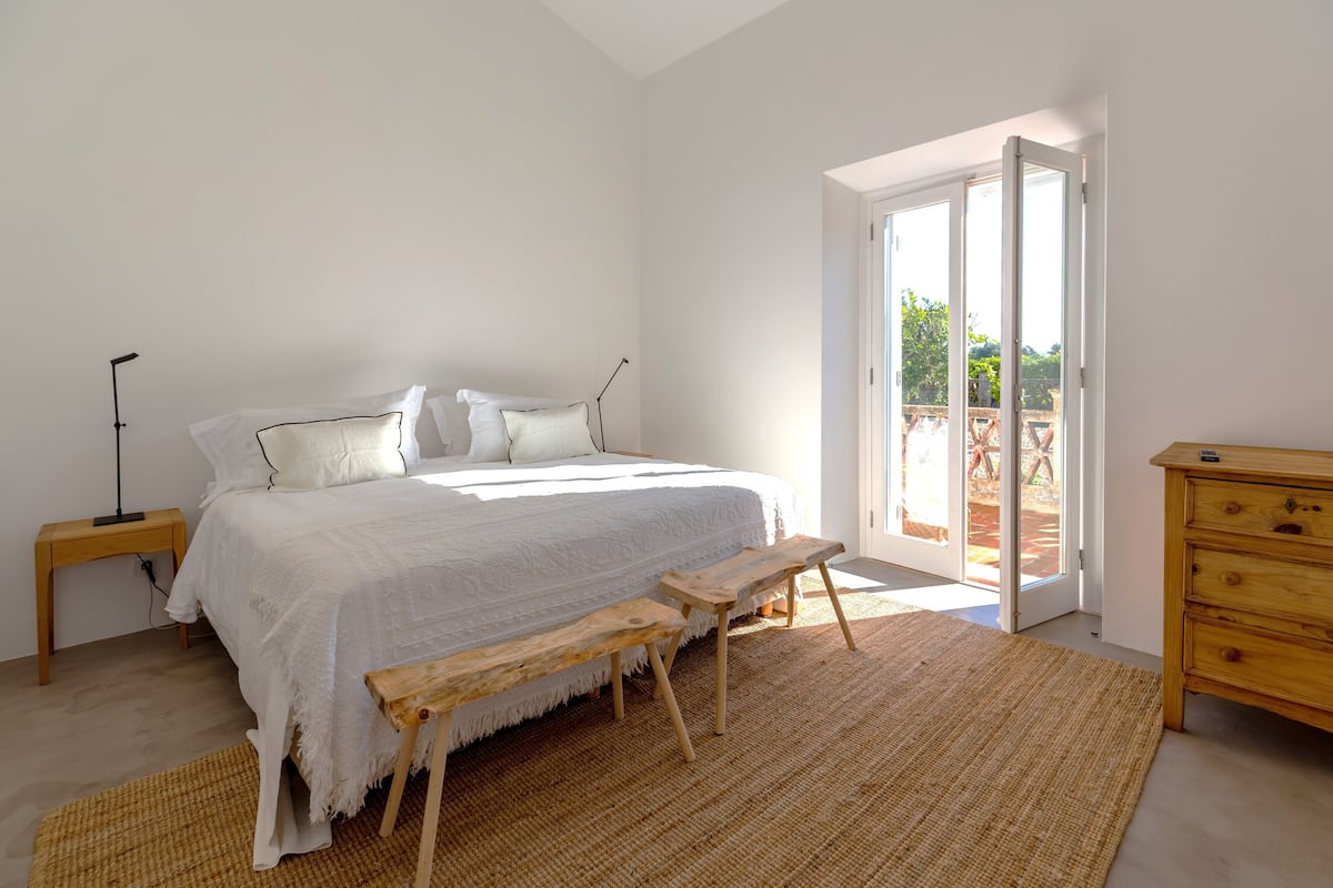 A bedroom with a large bed, wooden bench, and a dresser.