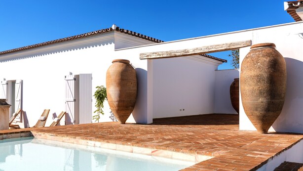 A pool area with large terracotta pots, a white building, and a clear blue sky. - Cenoura-Brava Villas & Suites. (Évora)