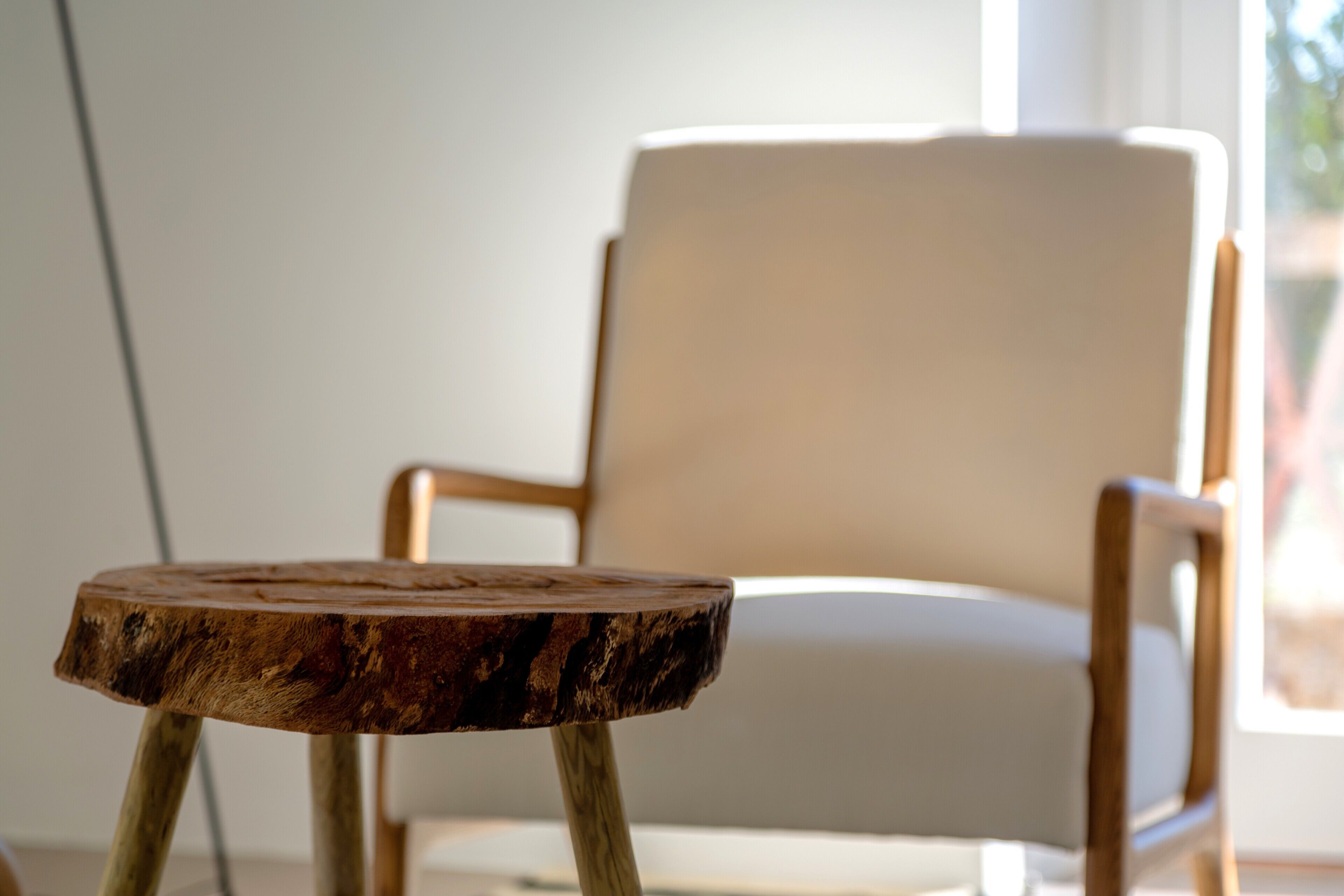 A wooden table with a natural finish in a room with a white chair and a window.