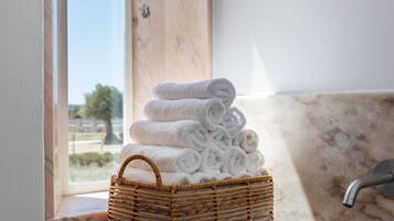 A bathroom with a marble sink, a wicker basket with folded towels, and a view of the outdoors through a window.