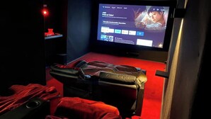 A movie theater with a red carpet, reclining seats, and a large screen displaying a film. - Le Ciné'ppart Easy Life (Bourgoin-Jallieu)