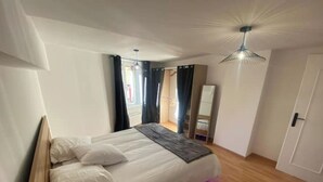 A bedroom with a bed, wooden headboard, a bedside table, a mirror, and a ceiling fan. - Le Ciné'ppart Easy Life (Bourgoin-Jallieu)