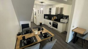 A compact kitchen with a dining area, including a table set for two, a washing machine, and a microwave. - Le Ciné'ppart Easy Life (Bourgoin-Jallieu)