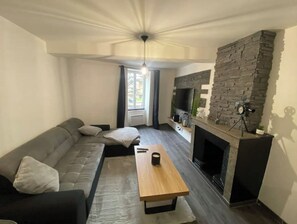 A modern living room with a stone fireplace, a sofa, a coffee table, and a TV. - Le Ciné'ppart Easy Life (Bourgoin-Jallieu)