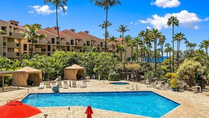 Un área de piscina de resort con varias piscinas, sillas de descanso y palmeras.