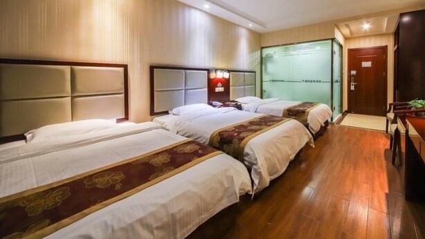 Une chambre d’hôtel avec trois lits, un plancher en bois, un téléviseur fixé au mur et une porte avec un panneau de verre.