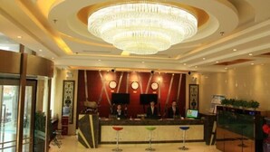 Un hall d’hôtel comprenant un grand lustre, un comptoir d’accueil et un espace détente avec des tabourets.