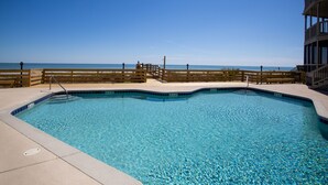 En klar, blå swimmingpool med træterrasse og træhegn, med udsigt over havet.