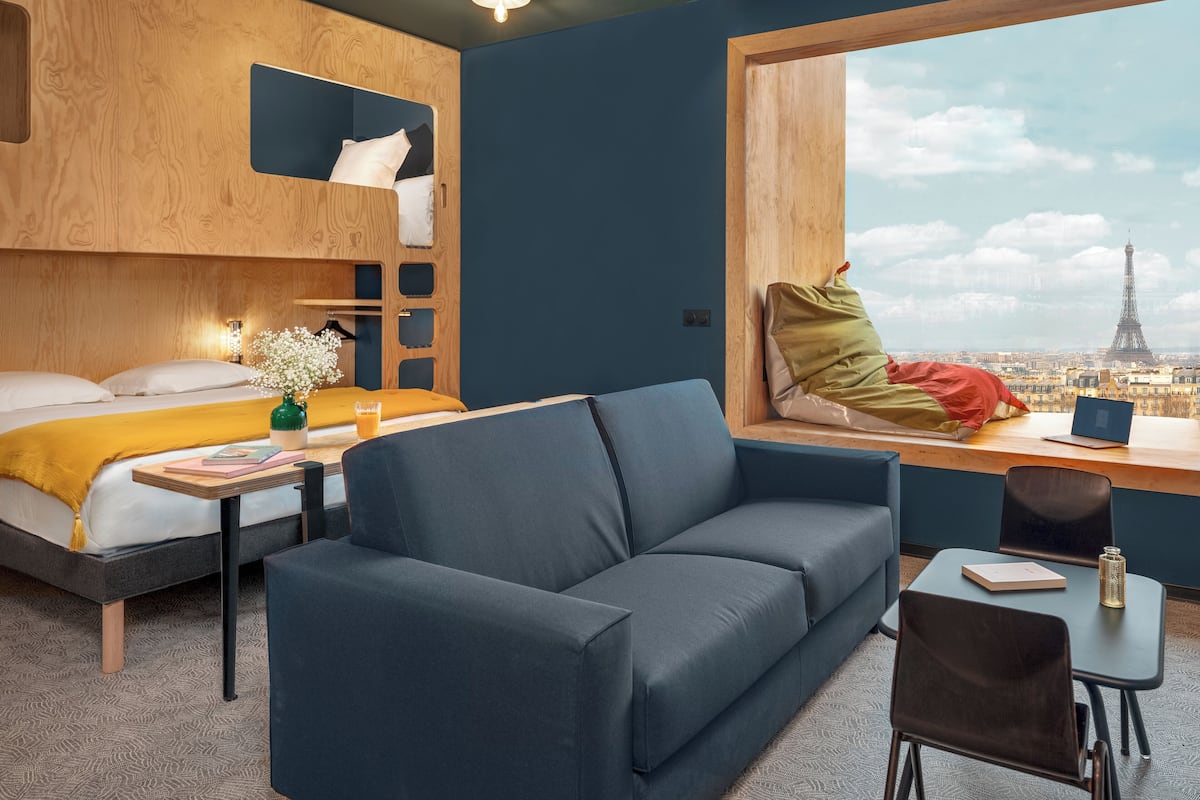 Ein modernes Zimmer mit Etagenbett, Sofa, Schreibtisch und Blick auf den Eiffelturm.
