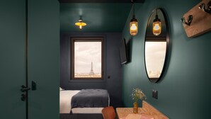 Un dormitorio con vistas a la Torre Eiffel, una cama, un escritorio con libros y un espejo en la pared.