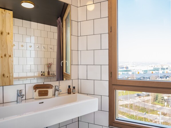 Un baño con un lavamanos blanco, un espejo y un ventanal con vistas a la ciudad.