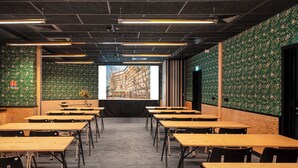 Un salón de conferencias con varias mesas y sillas, paredes de diseño verde y una pantalla de proyección al frente.